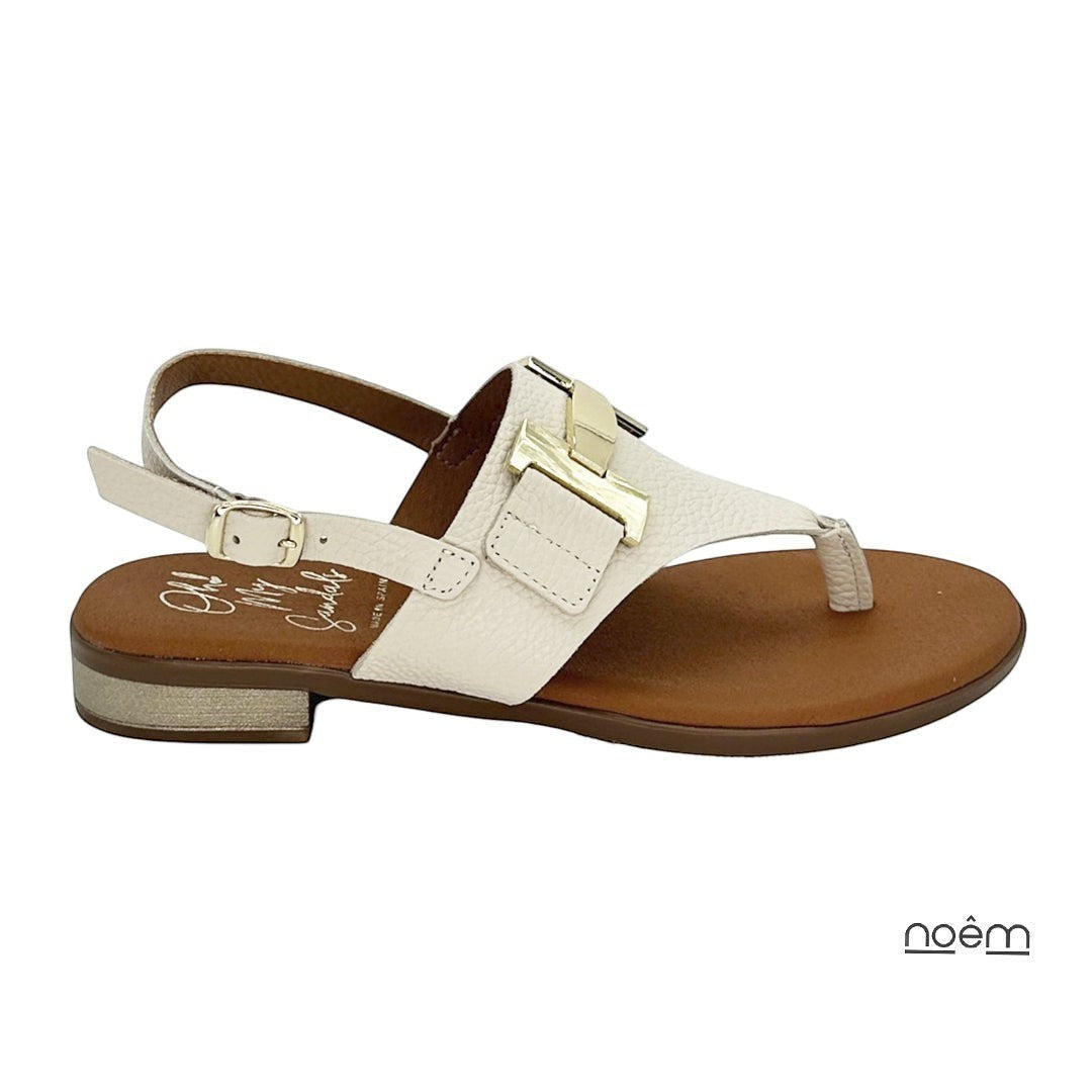 Sandalia plana beige de piel con detalle metálico dorado y tira trasera ajustable de Noêm & Seque. Elegancia minimalista.