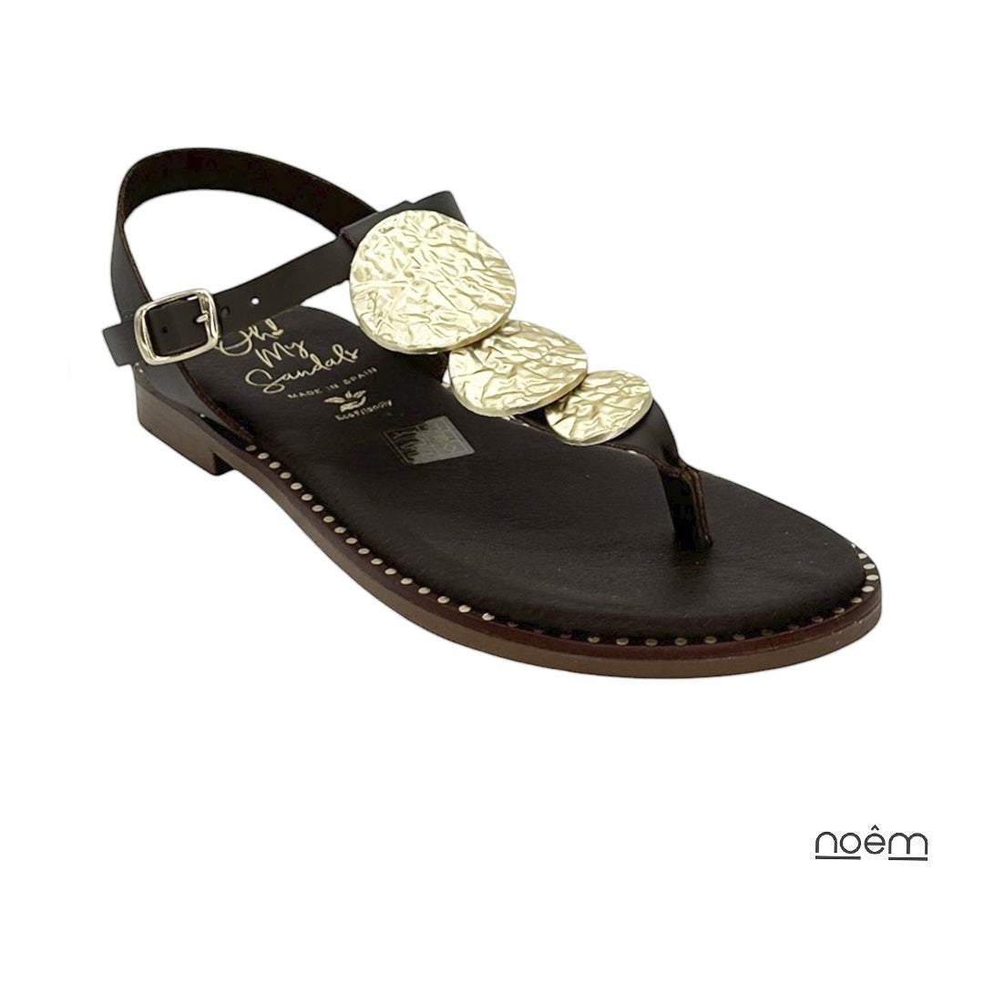 Sandalias planas negras de piel con detalle de discos dorados texturizados y cierre ajustable en el tobillo. Marca Noêm & Seque.